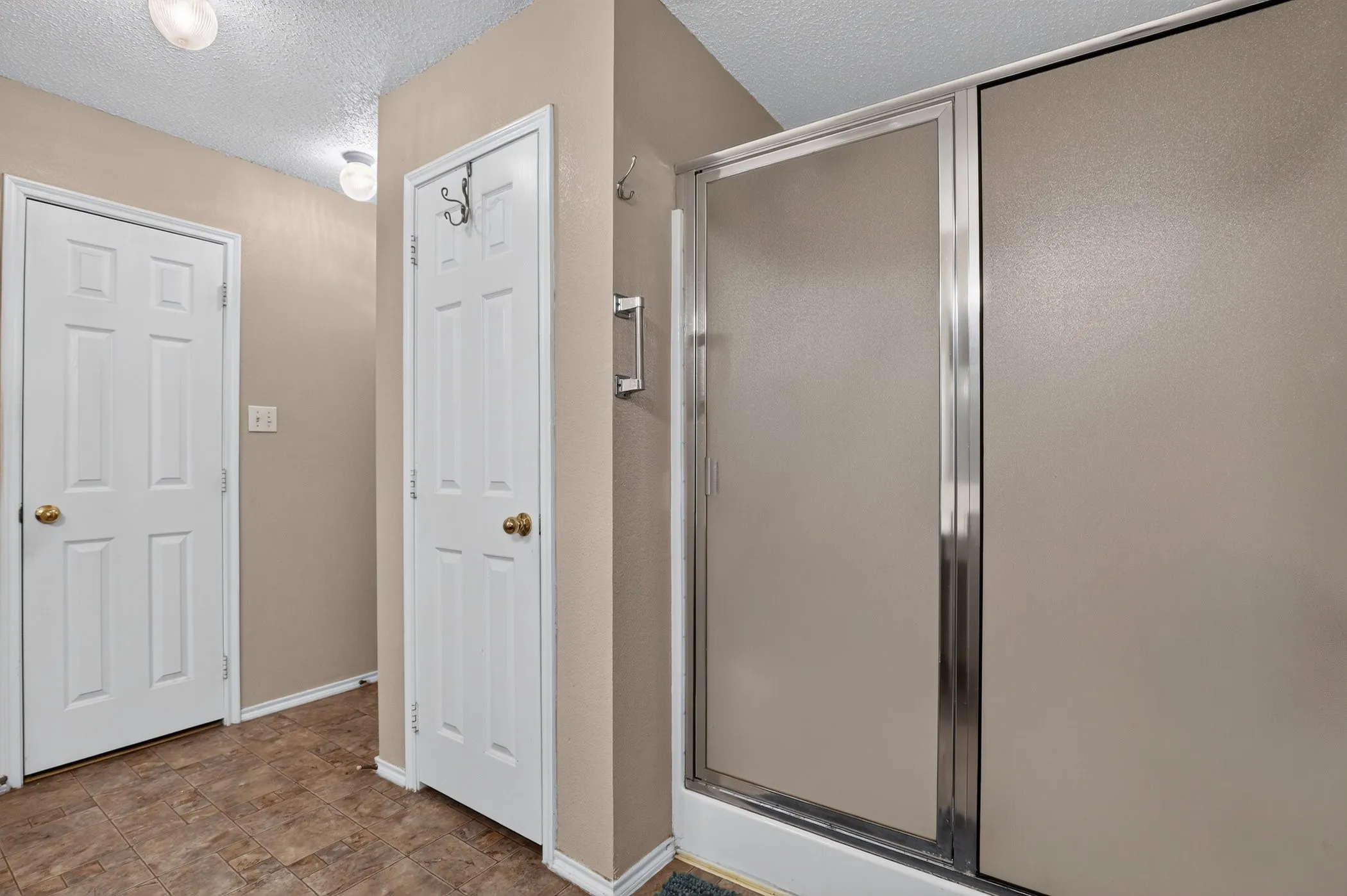 Enclosed shower with frosted glass doors, white six-panel doors with brass hardware, and wood-finish flooring