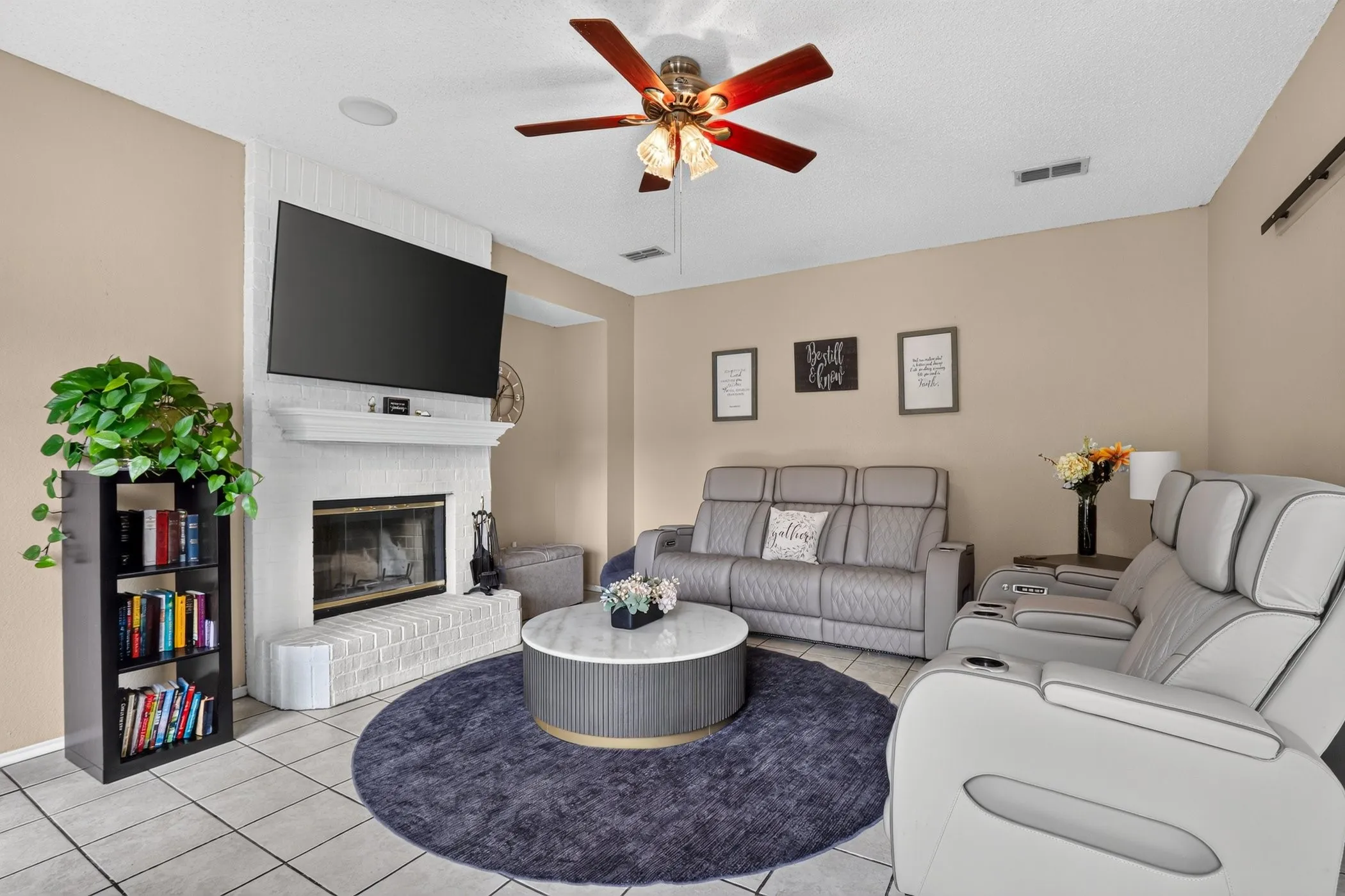 White brick fireplace with a mantel, mounted television, wood-finish ceiling fan, recessed lighting, and tile flooring