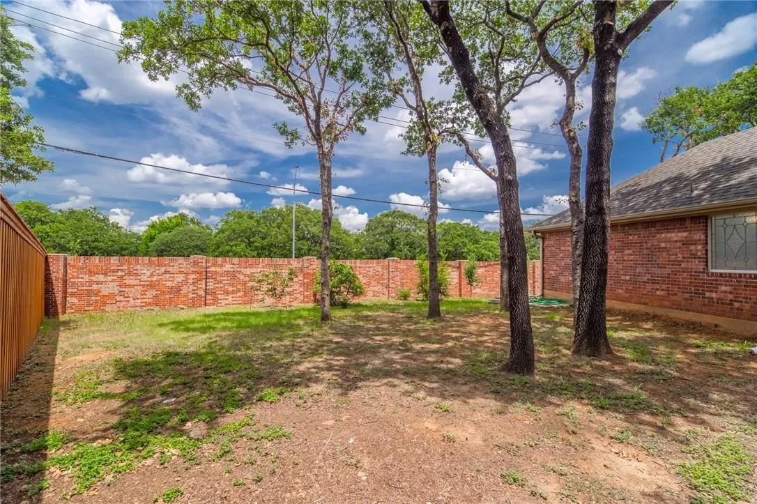 Expansive yard featuring mature trees, a full brick perimeter wall, and a wood-paneled fence