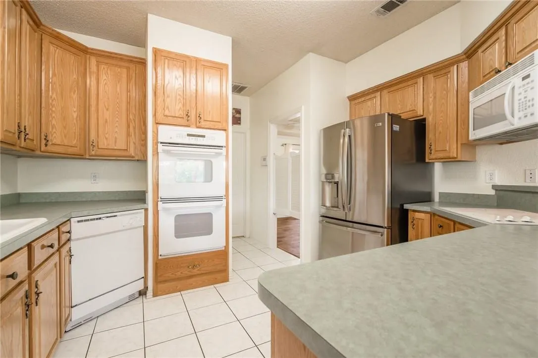 Kitchen featuring wood cabinetry, white tile flooring, stainless steel refrigerator, white built-in double oven, and a white dishwasher