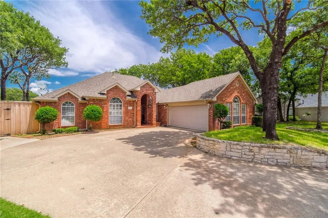 Brick exterior with arched windows, attached garage, concrete driveway, and stone retaining wall