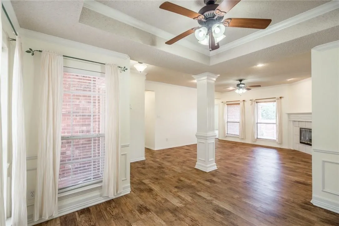 Wood-finish flooring throughout, tray ceiling with a ceiling fan, and a decorative column