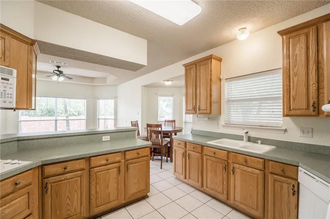 Kitchen with wood cabinetry, light-toned countertops, a built-in double basin sink, and tile flooring