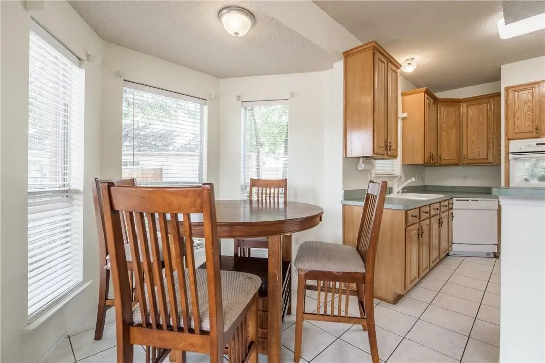Bay window with blinds, recessed lighting, tile flooring, oak cabinetry, and integrated appliances