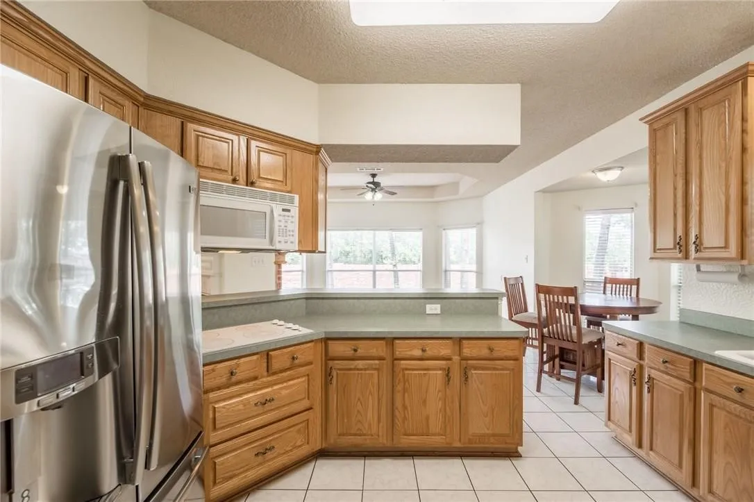 Kitchen featuring wood cabinetry, stainless steel refrigerator, built-in microwave, light-toned countertops, and tile flooring