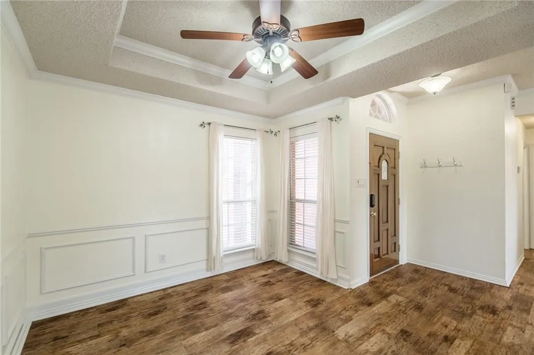 Tray ceiling with crown molding, wood-finish flooring, wainscoting, and a decorative front door with an arched transom