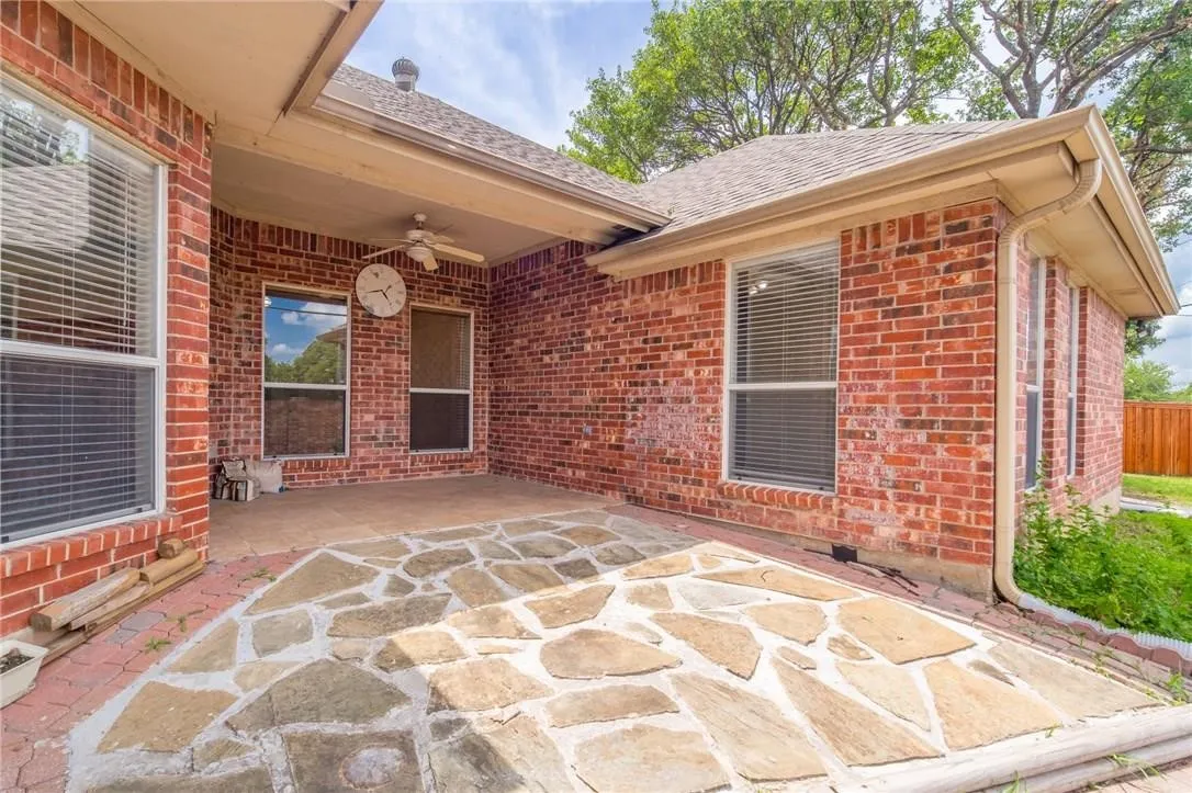 Covered patio featuring a stone slab surface, brick exterior, and a ceiling fan