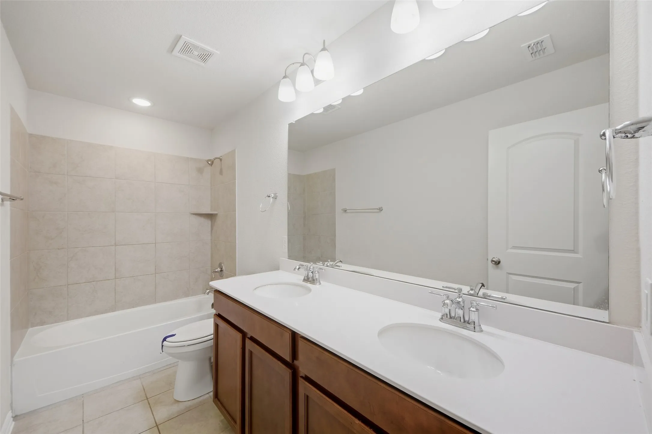 Double vanity with integrated sinks, a large wall-mounted mirror, and a combination tub and shower with tile surround