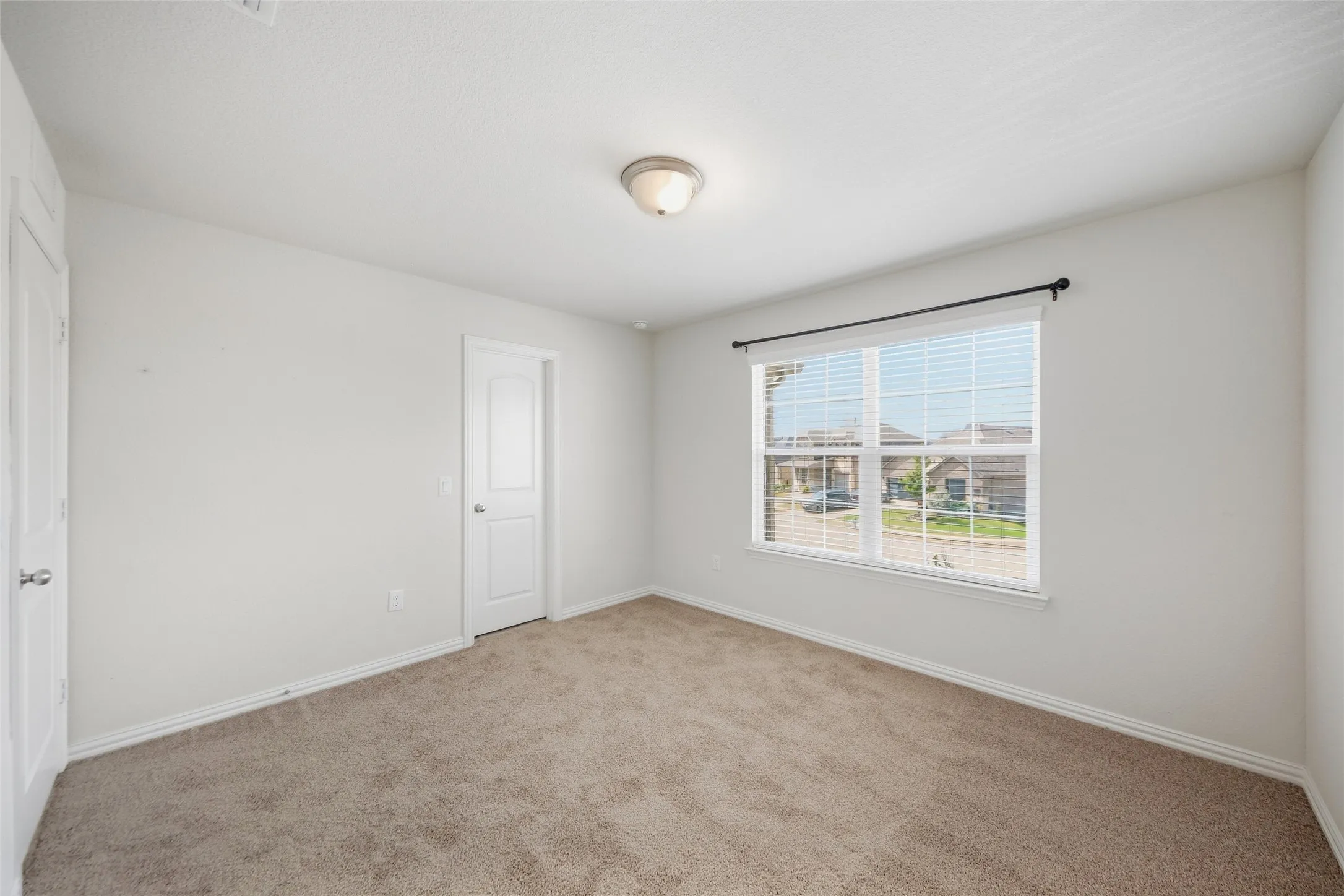 Carpeted room with white walls, a large window with blinds, and white doors