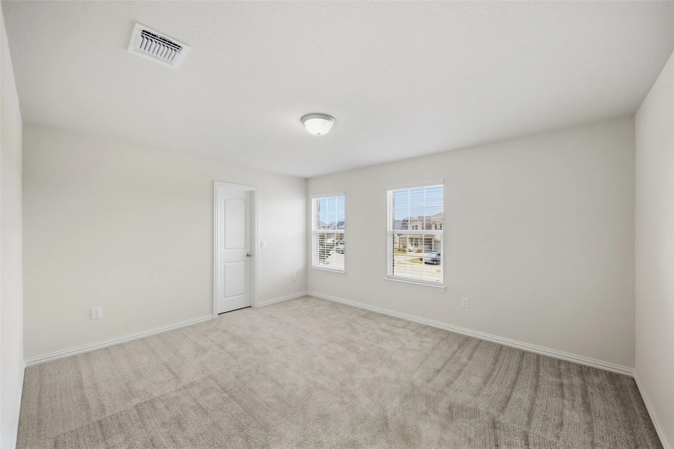 Neutral wall paint with carpet flooring, two windows with blinds, and an overhead flush-mount light fixture