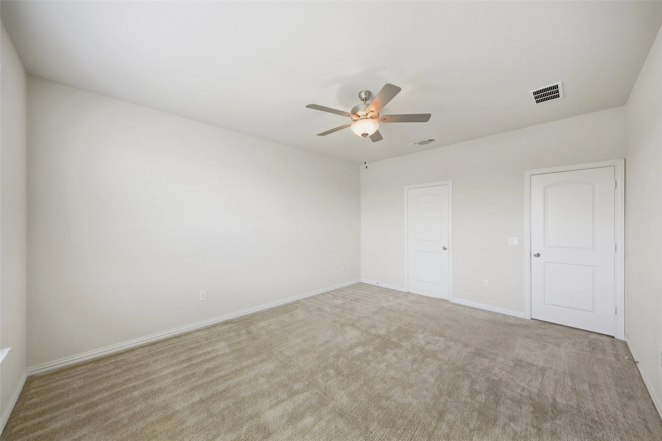 Spacious room featuring neutral carpeting, a ceiling fan with integrated lighting, and two panel doors