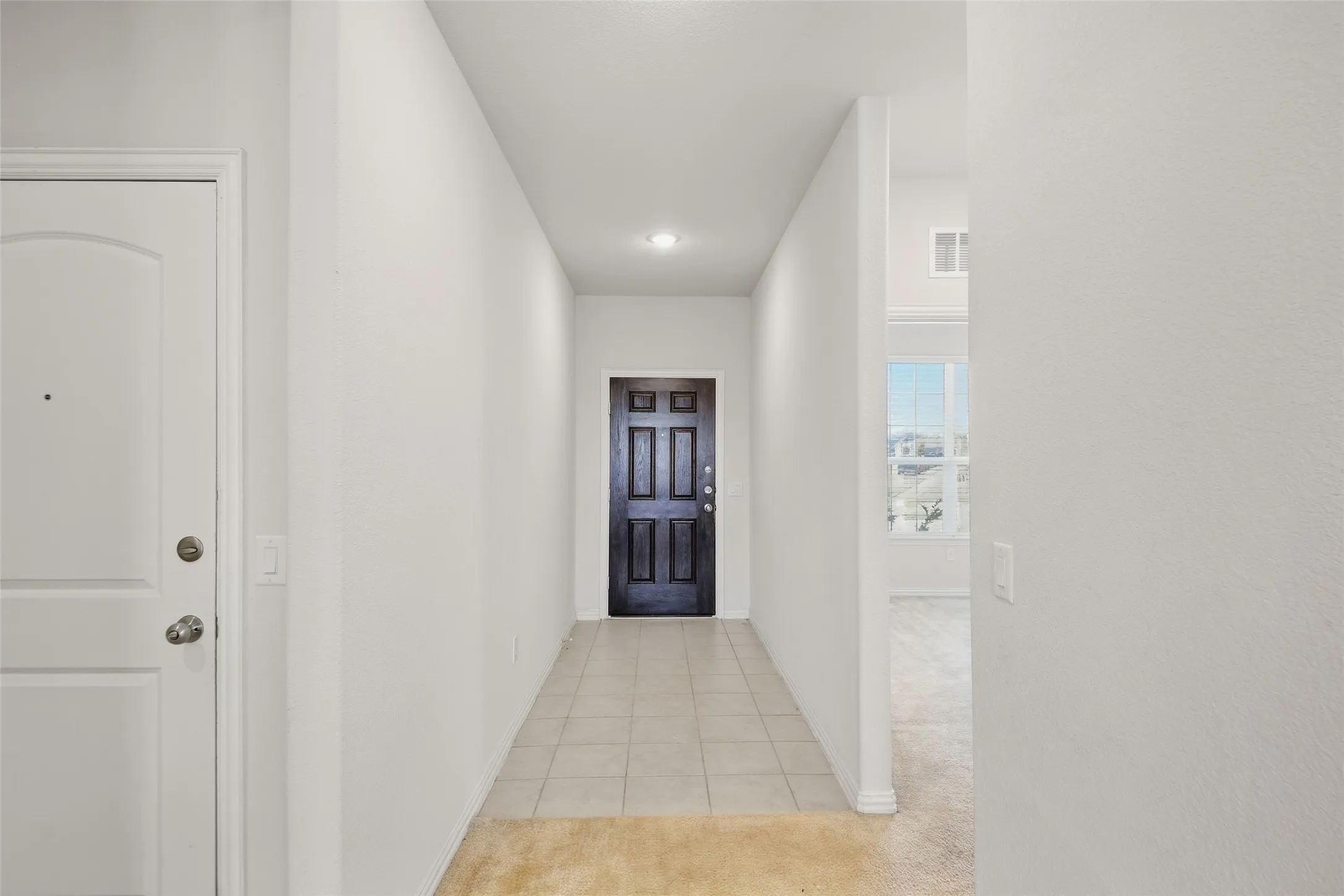 Recessed lighting illuminates the tiled entry hallway with a paneled dark wood-finish door