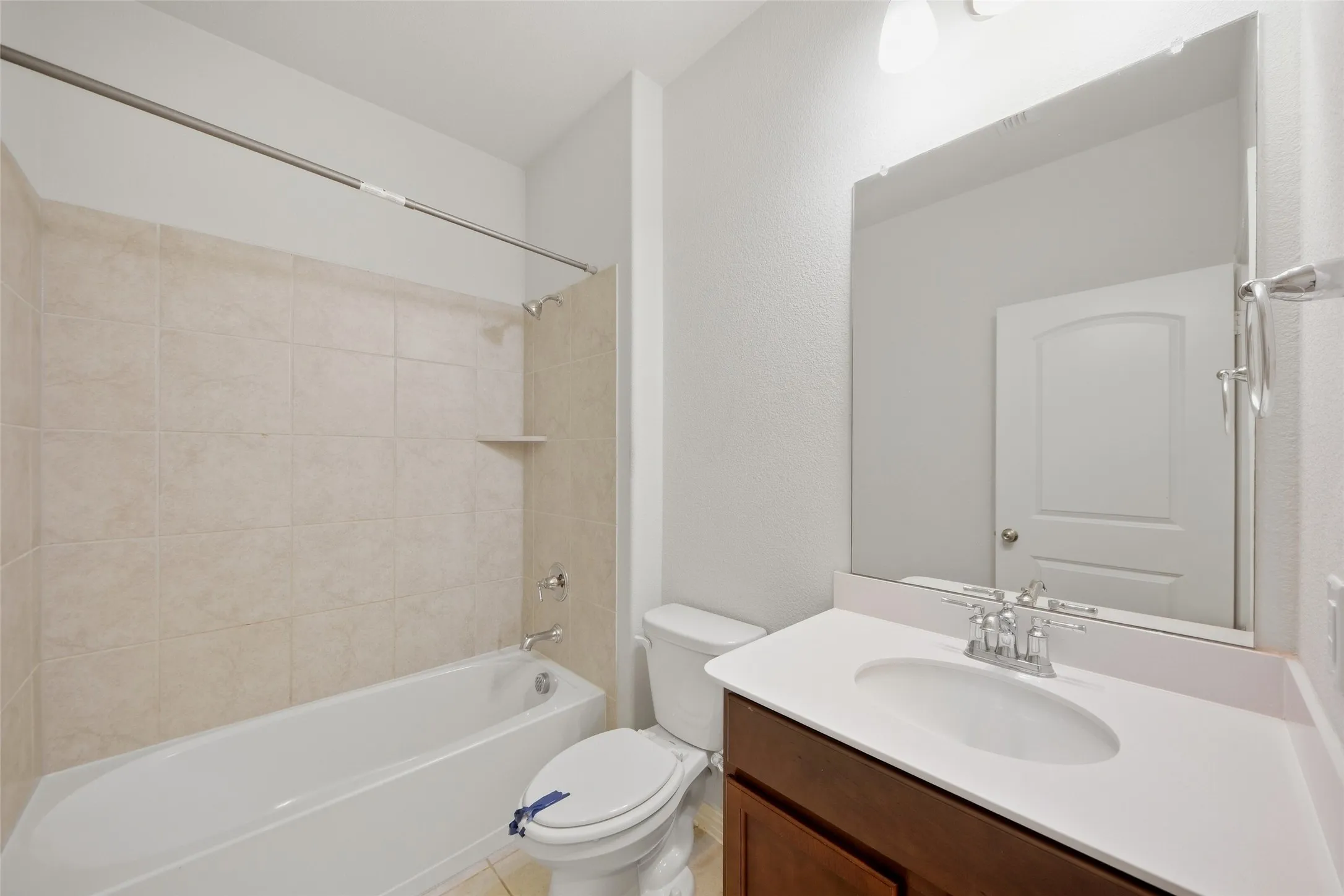 White bathtub with tiled surround, single vanity with integrated sink, white countertop, and dark wood-finish cabinetry