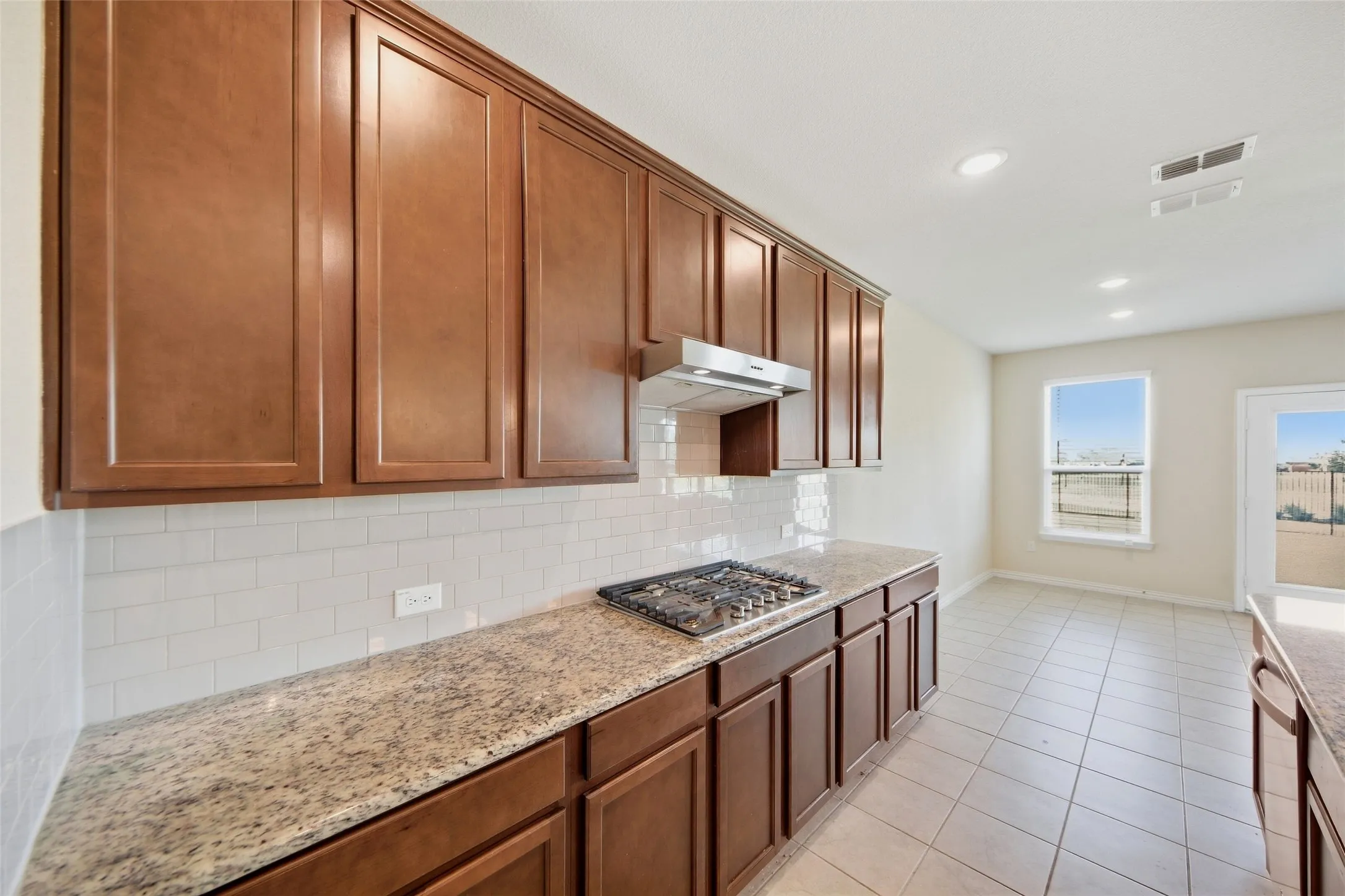 Kitchen featuring rich wood cabinetry, patterned stone countertops, a gas cooktop, subway tile backsplash, and recessed lighting