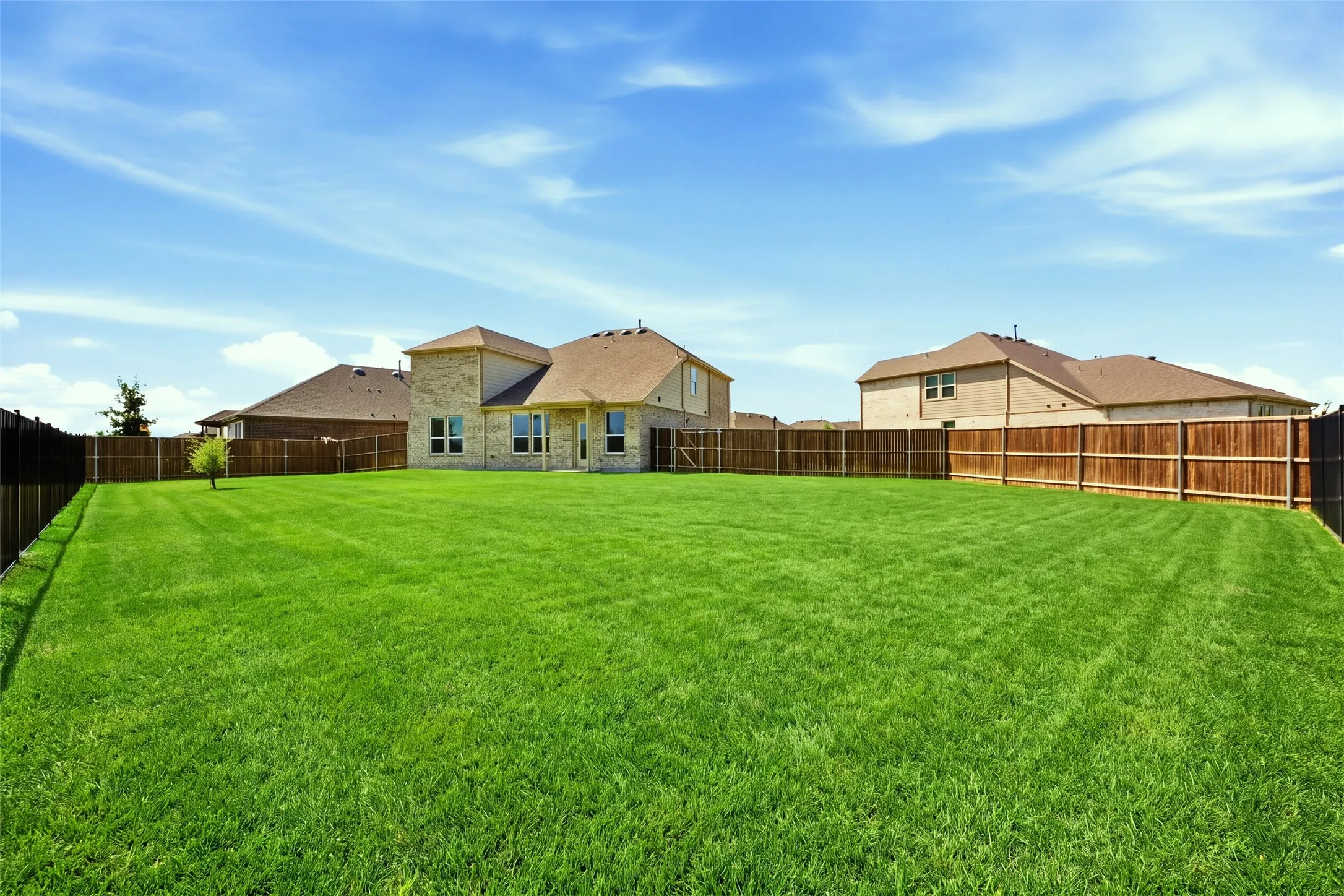 Expansive backyard featuring a manicured lawn, full wood fencing, and a two-story home with a stone and siding exterior