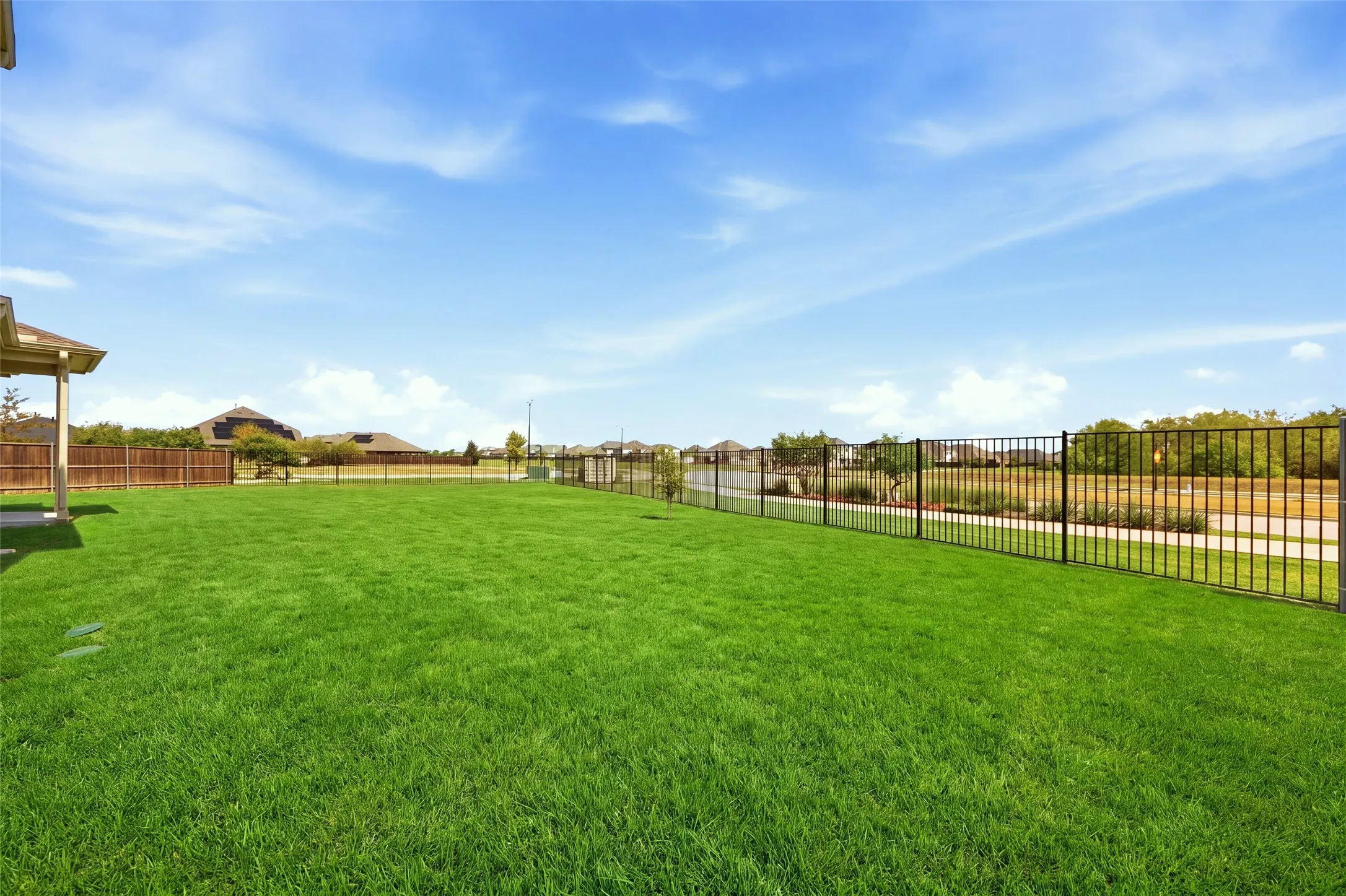 Expansive lawn with a black metal fence and a wood-panel fence