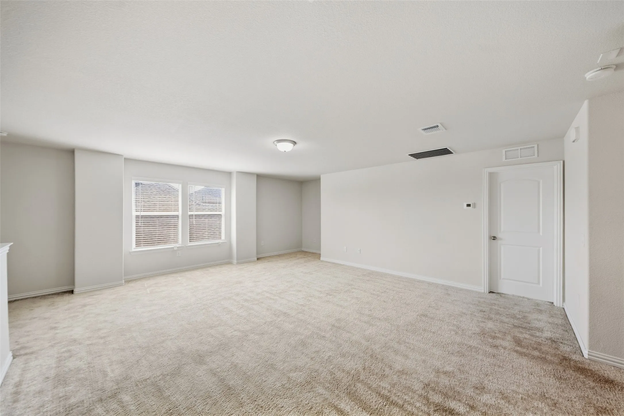 Spacious room with light-toned carpeting, white walls, and a pair of windows