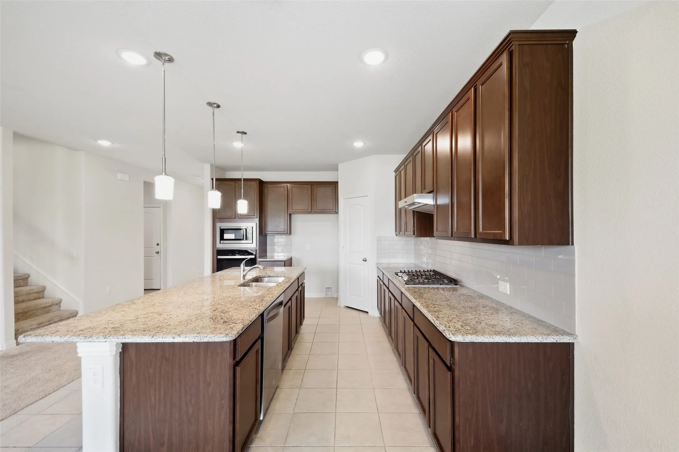 Kitchen featuring a long center island, dark wood-finish cabinetry, light-toned countertops, tile flooring, and integrated stainless steel appliances