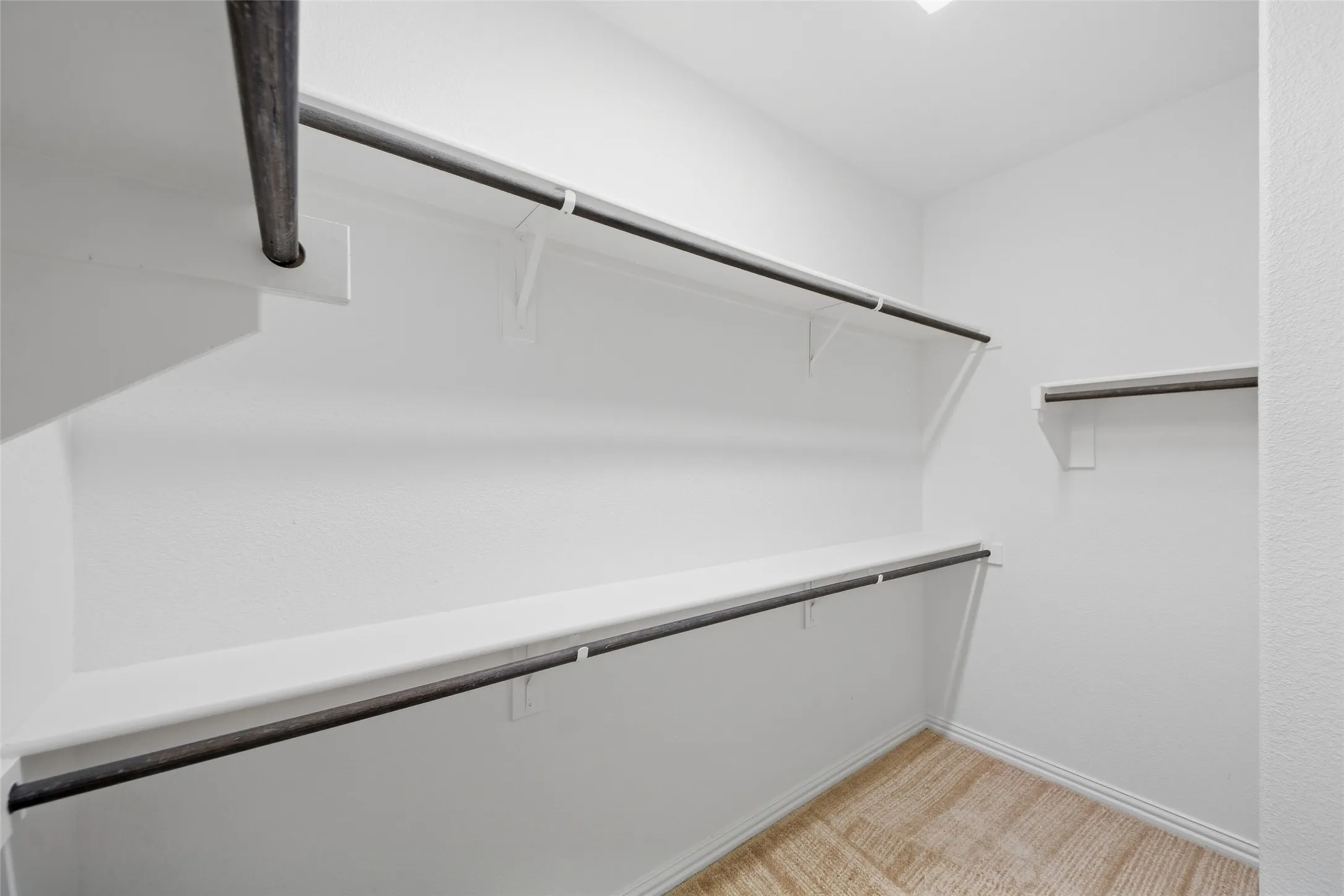 Walk-in closet with multiple hanging rods, shelving, white walls, and wood-finish flooring