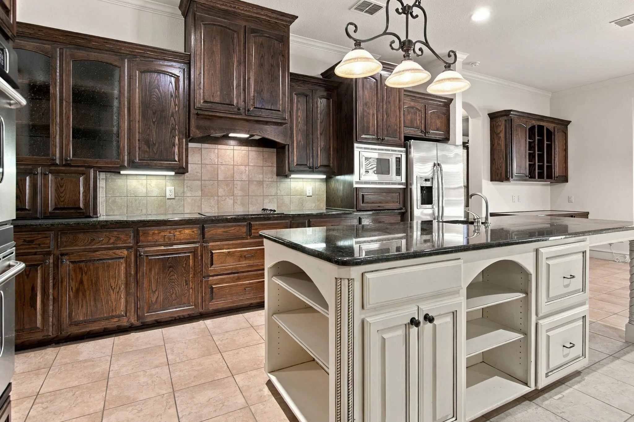 Kitchen featuring dark wood cabinetry, a central island with integrated shelving, dark countertops, stainless steel appliances, and tile flooring
