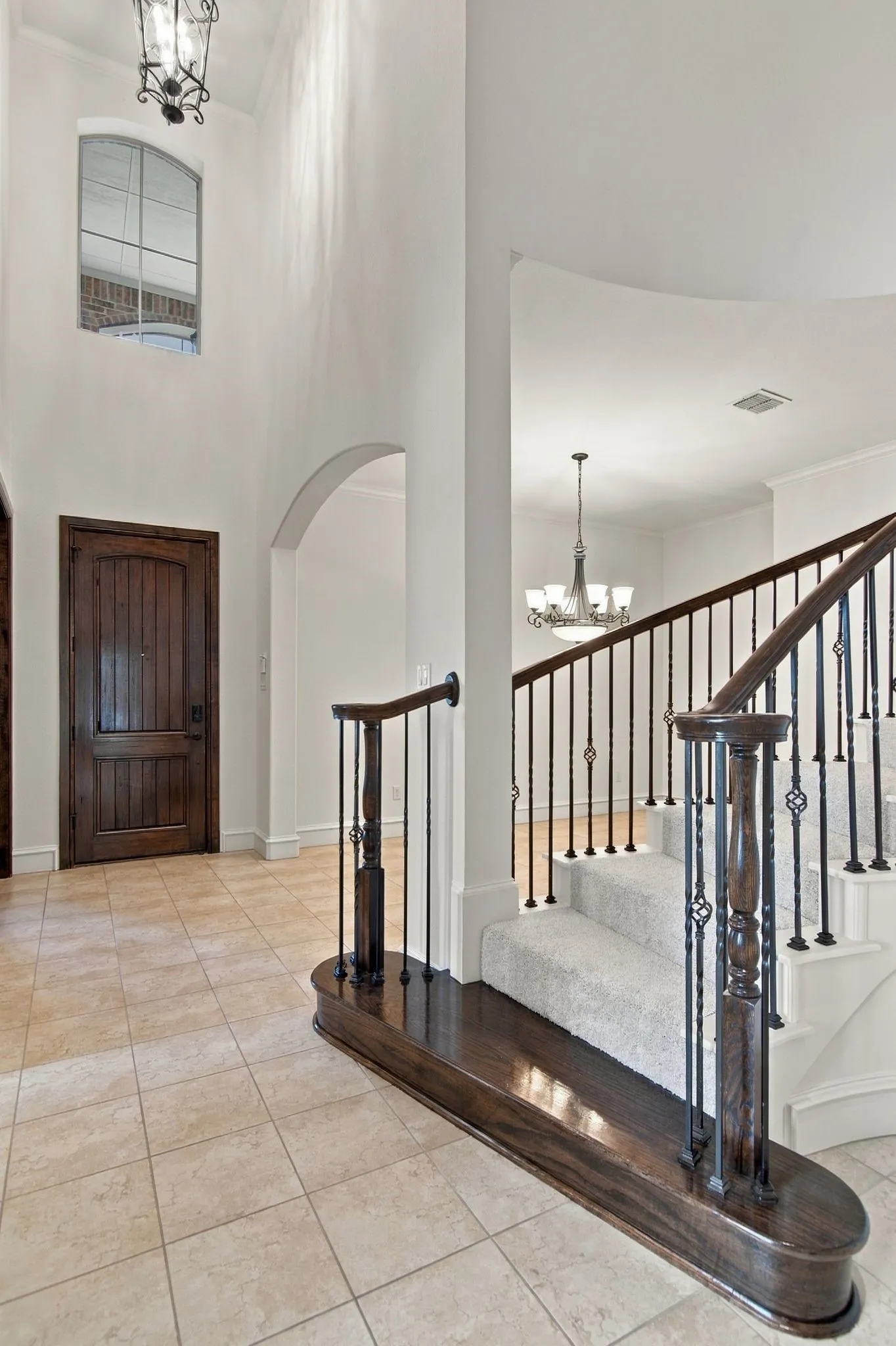Foyer featuring high ceilings, arched doorway, tile flooring, and a grand staircase with dark wood newel posts and iron balusters