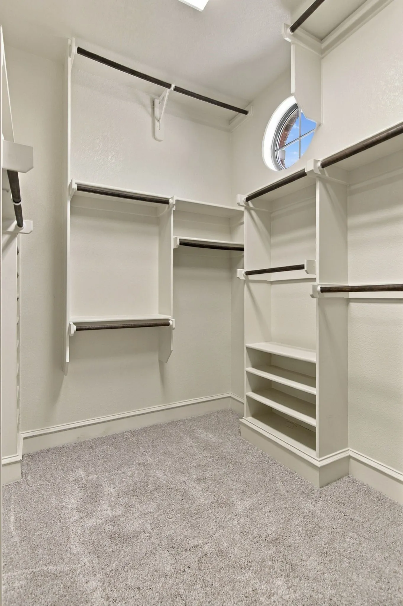 Built-in shelving and hanging rods, built-in shoe rack, round window, and light gray carpeting