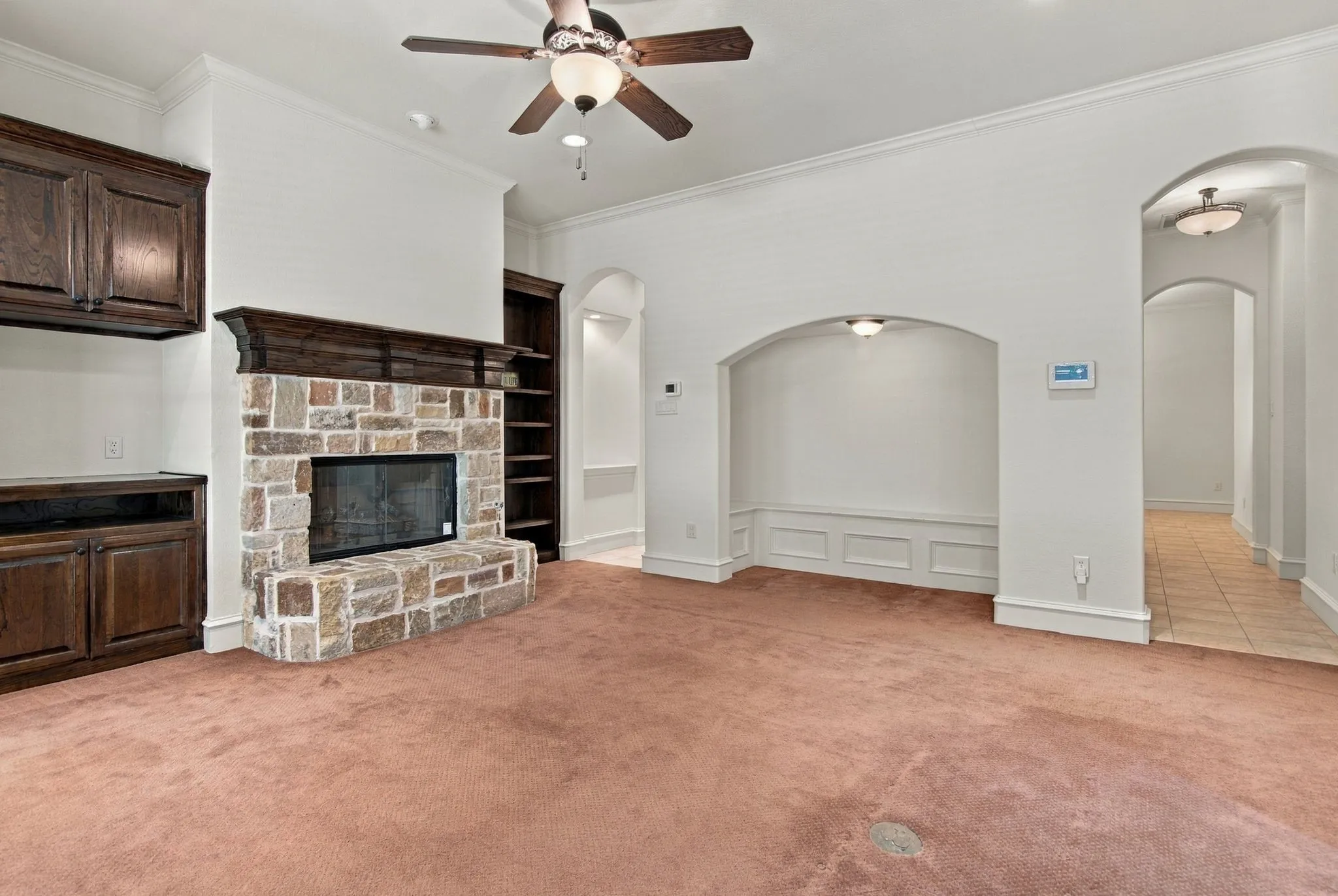 Stone-faced fireplace with a wood mantle, built-in cabinetry, arched wall alcove, and ceiling fan