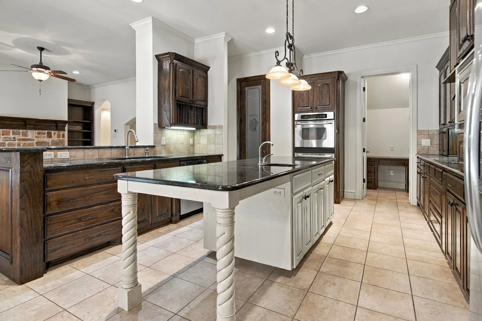 Kitchen featuring dark wood cabinetry, a central island with carved legs, stainless steel built-in appliances, and tile flooring