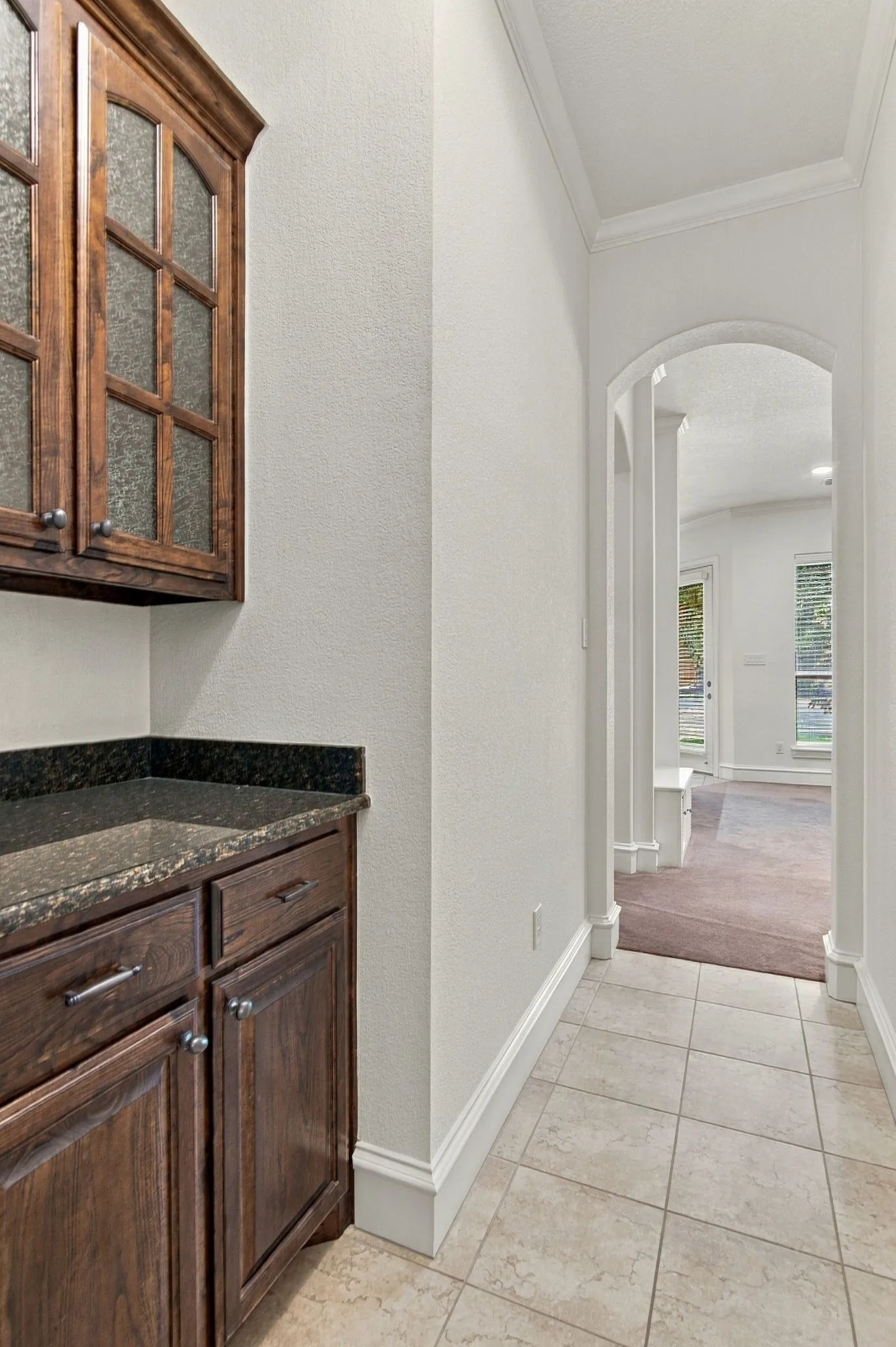 Built-in cabinetry with glass panel doors, dark countertop, and tile flooring