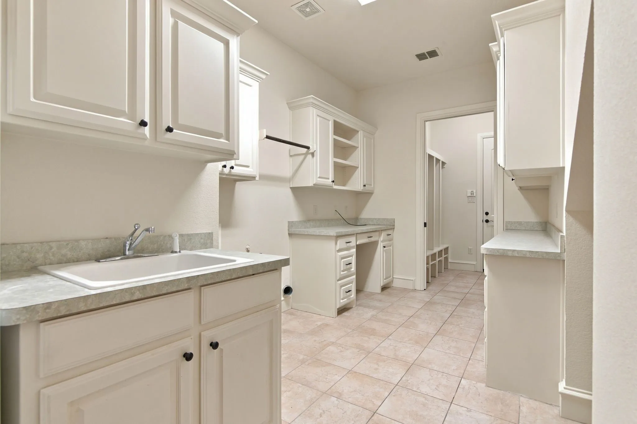 Utility room featuring white cabinetry, a built-in sink with a countertop, tiled flooring, and a dedicated desk area