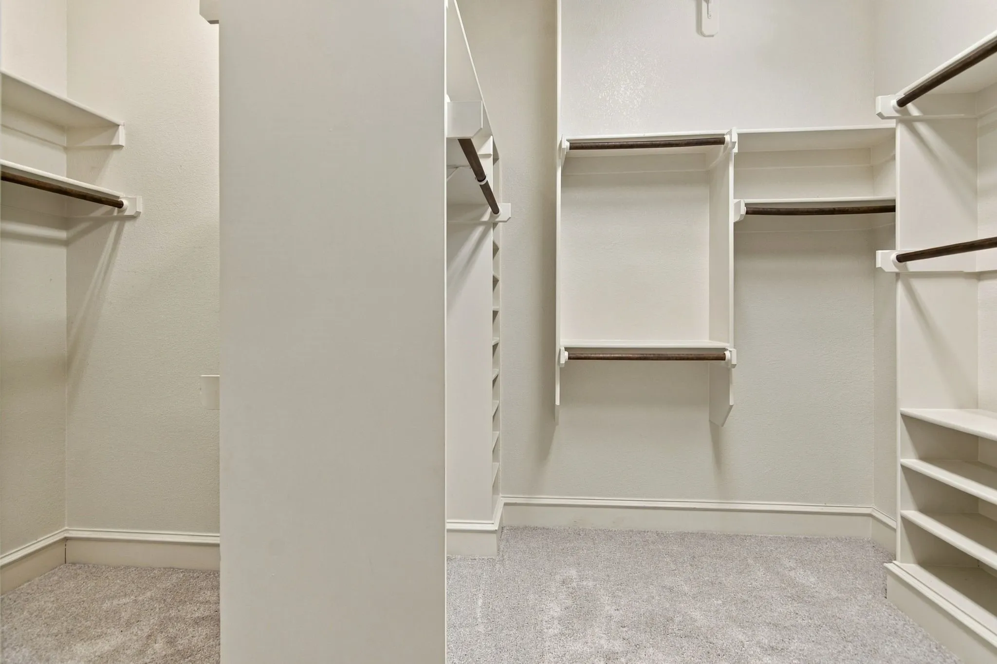 Spacious walk-in closet with multiple built-in shelving units, integrated hanging rods, and light-colored carpeting