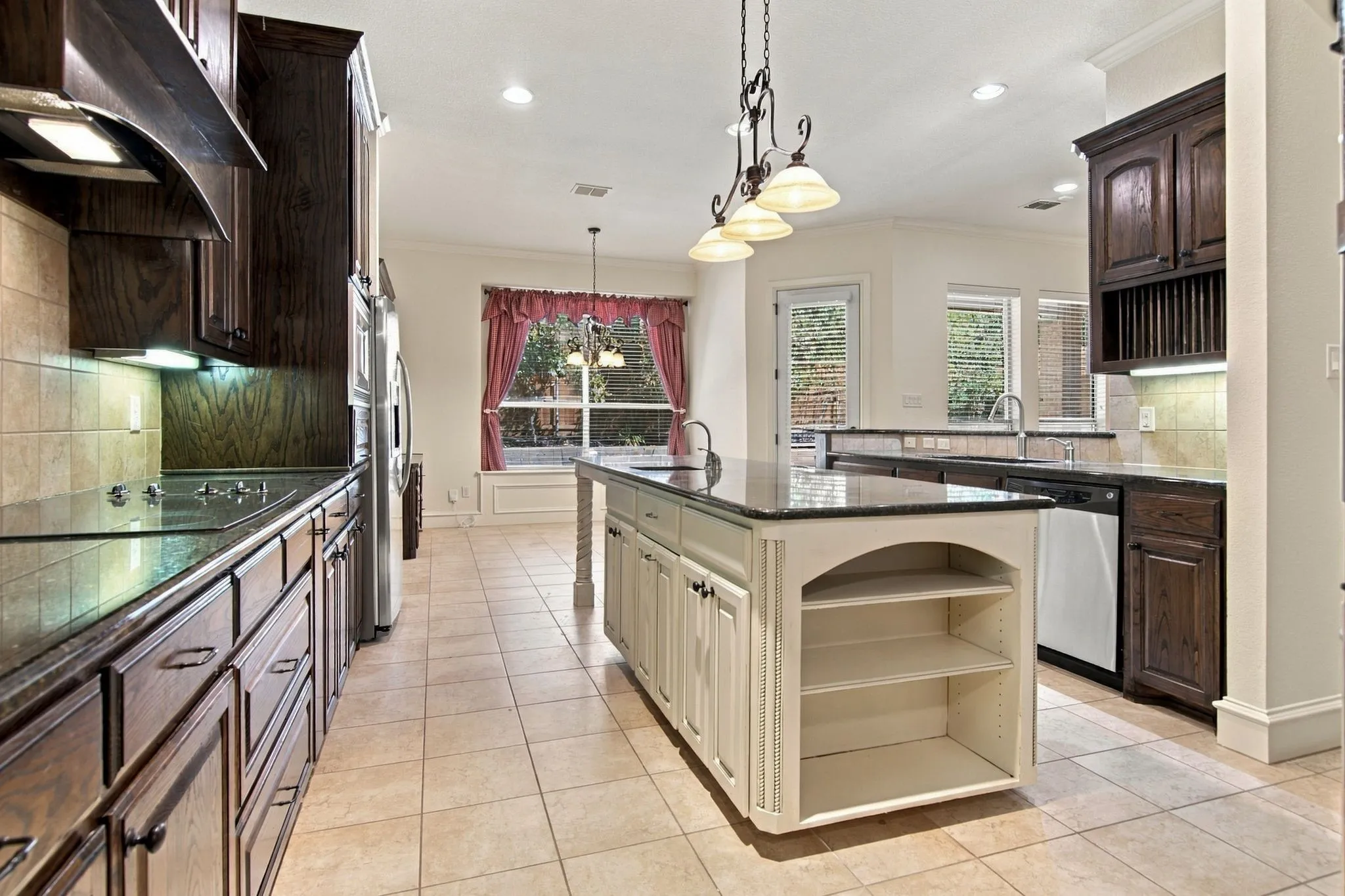 Spacious kitchen featuring an island with built-in shelving, dark wood cabinetry, stainless steel appliances, and tile flooring