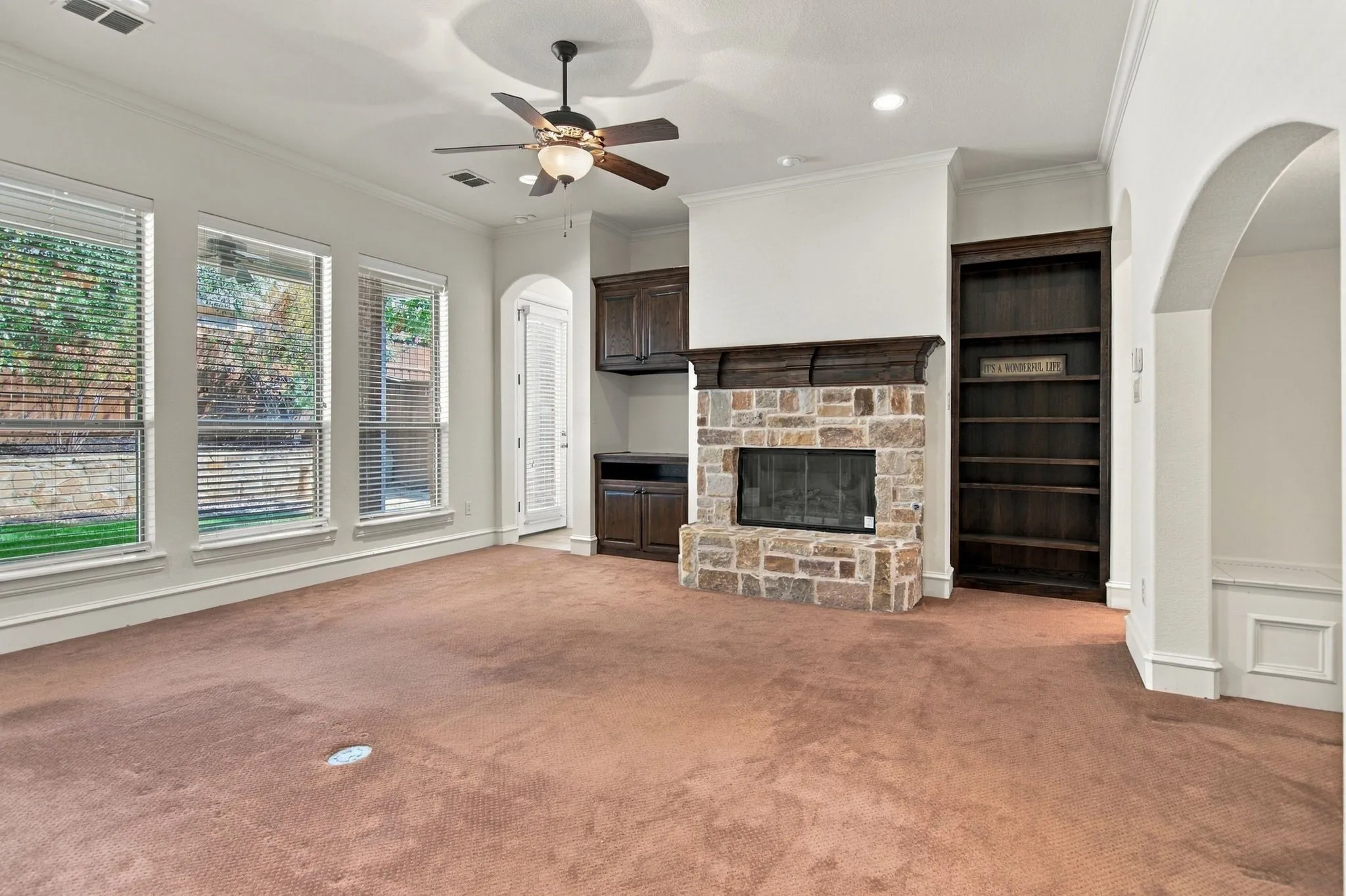 Stone-faced fireplace with a wood mantle, built-in shelving, dark wood-finish cabinetry, and multiple windows