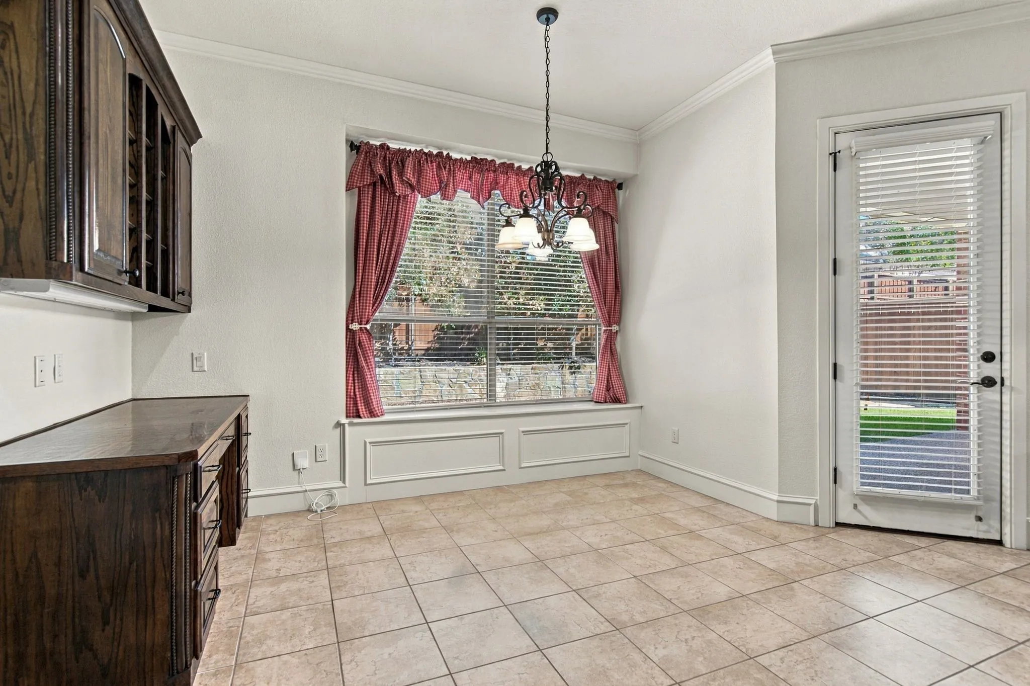 Built-in dark wood cabinetry with integrated wine rack, neutral tile flooring, window with decorative trim, and crown molding