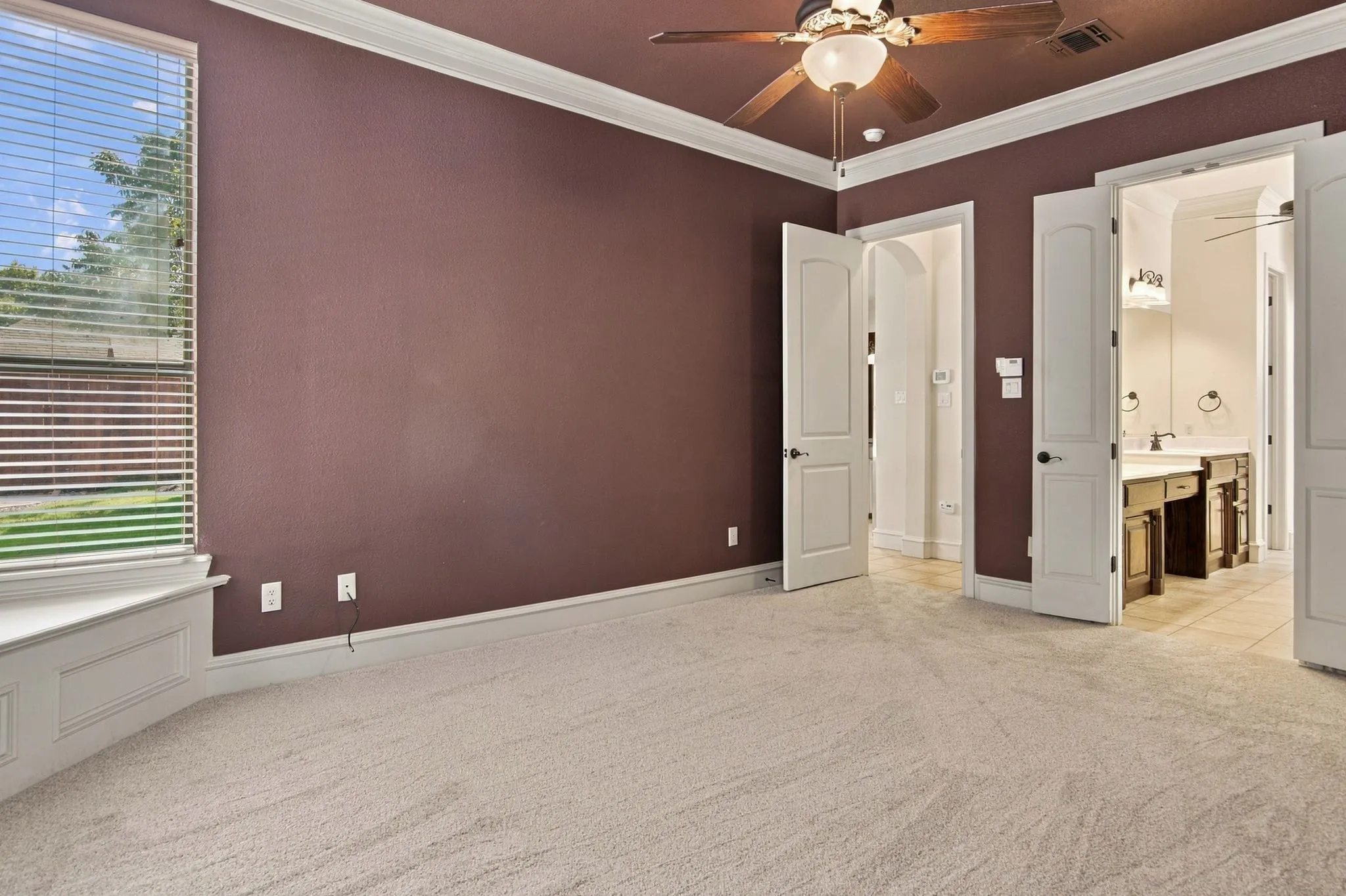 Neutral-toned carpeting, bay window with integrated seating, ceiling fan with integrated lighting, crown molding, and arched doorways