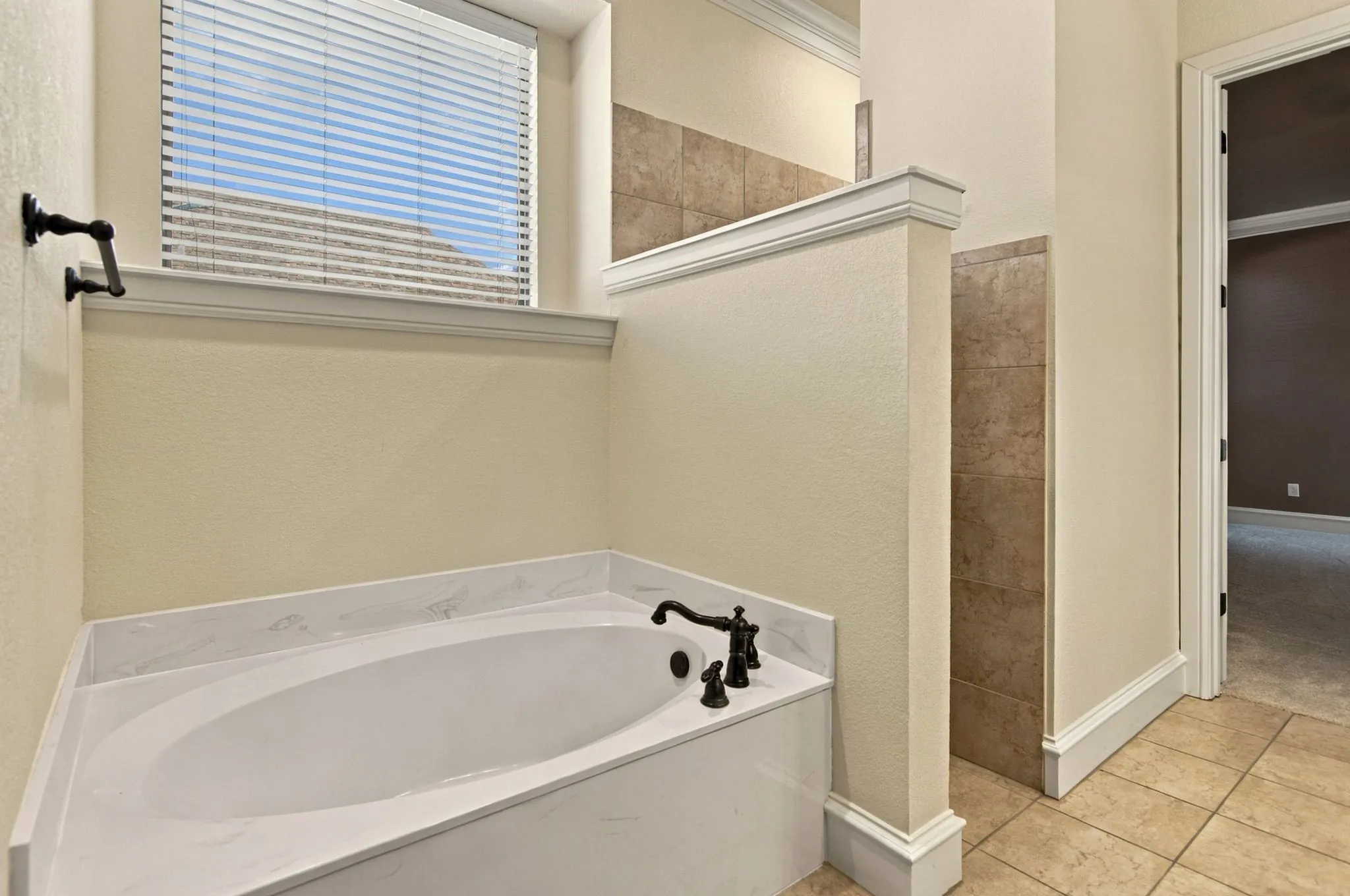 Built-in soaking tub with a white finish and dark bronze fixtures, framed by a window with blinds