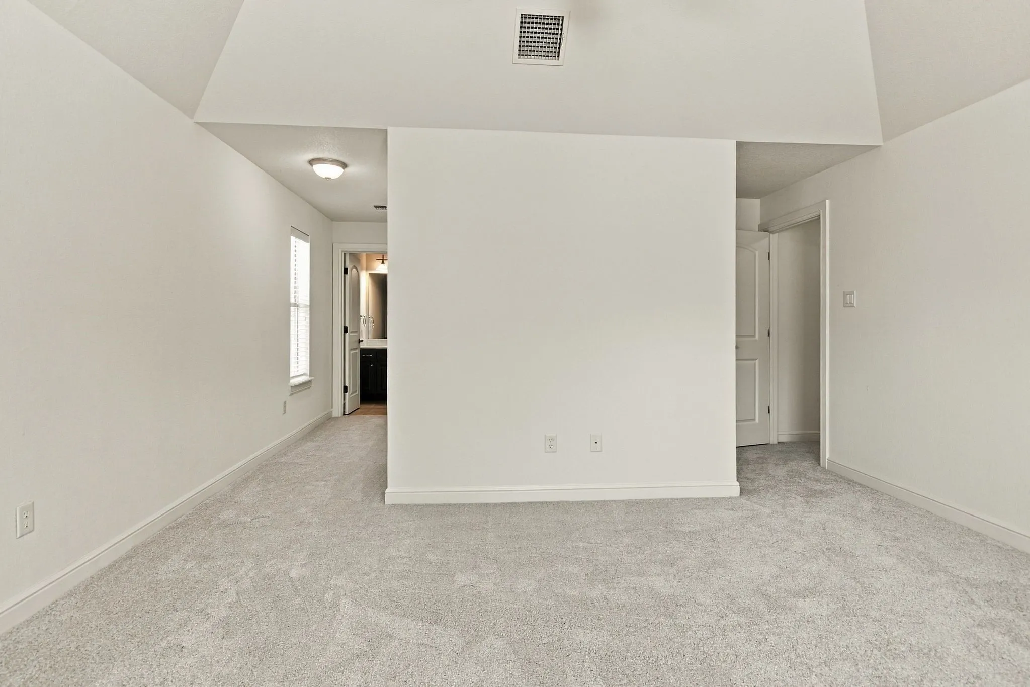 Vaulted ceiling with an overhead vent, light-toned carpeted flooring, and a white interior door
