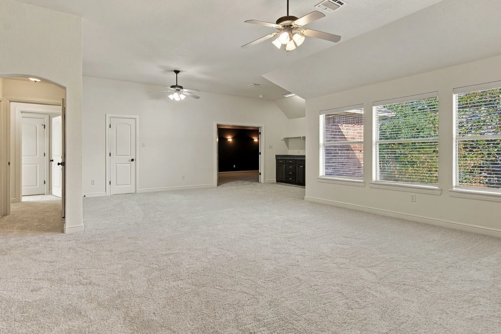 Spacious room with light-colored carpeting, multiple windows with blinds, and two ceiling fans