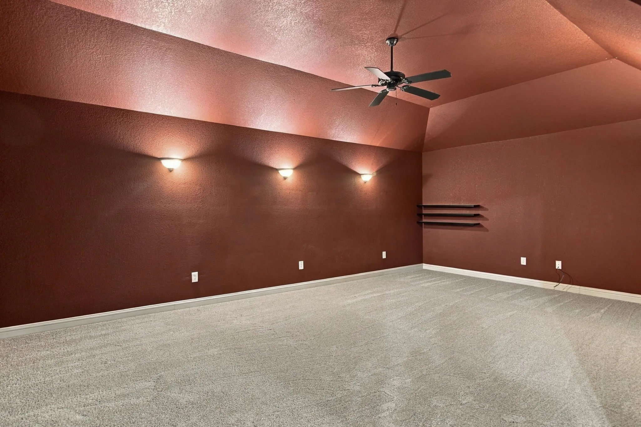 Vaulted ceiling with a ceiling fan, wall-mounted sconces, built-in shelving, and light gray carpet