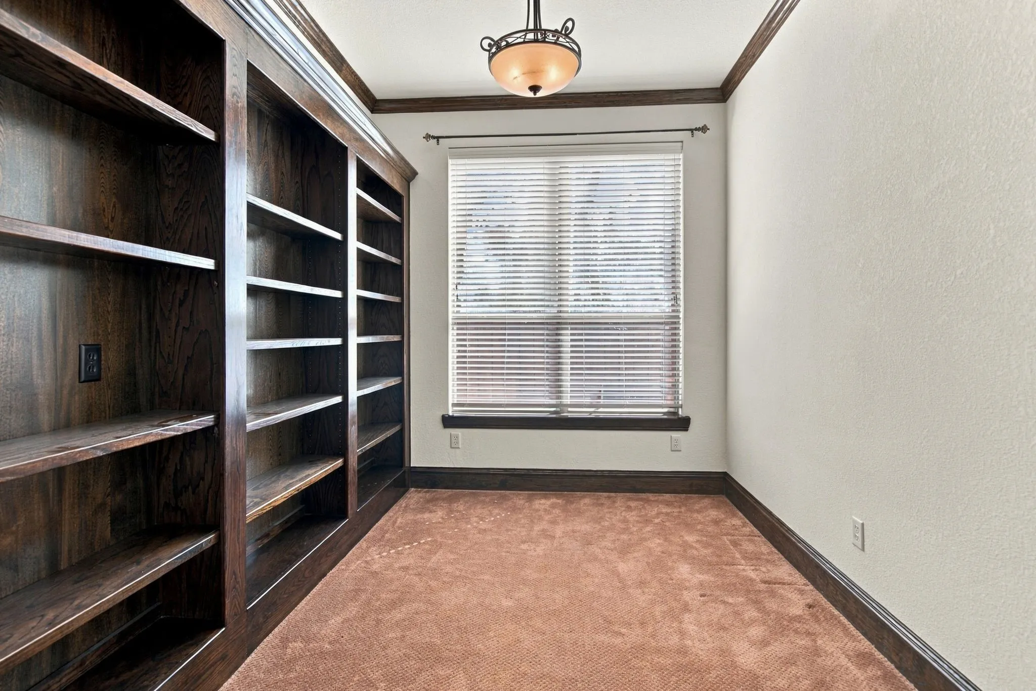 Built-in wood shelving, window with blinds, recessed ceiling light fixture, crown molding, and contrasting wood trim