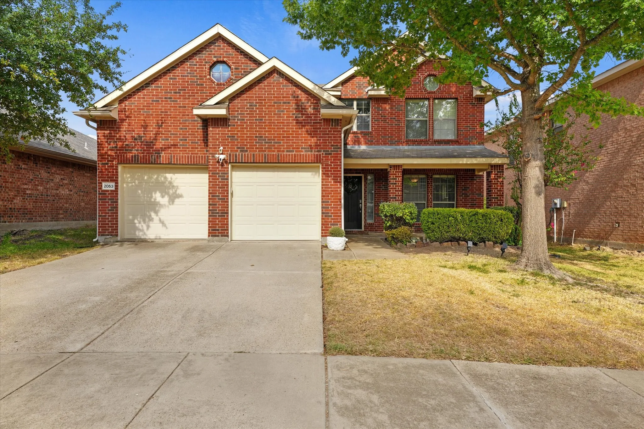 Red brick exterior with white trim, a covered entry porch, and a two-car garage