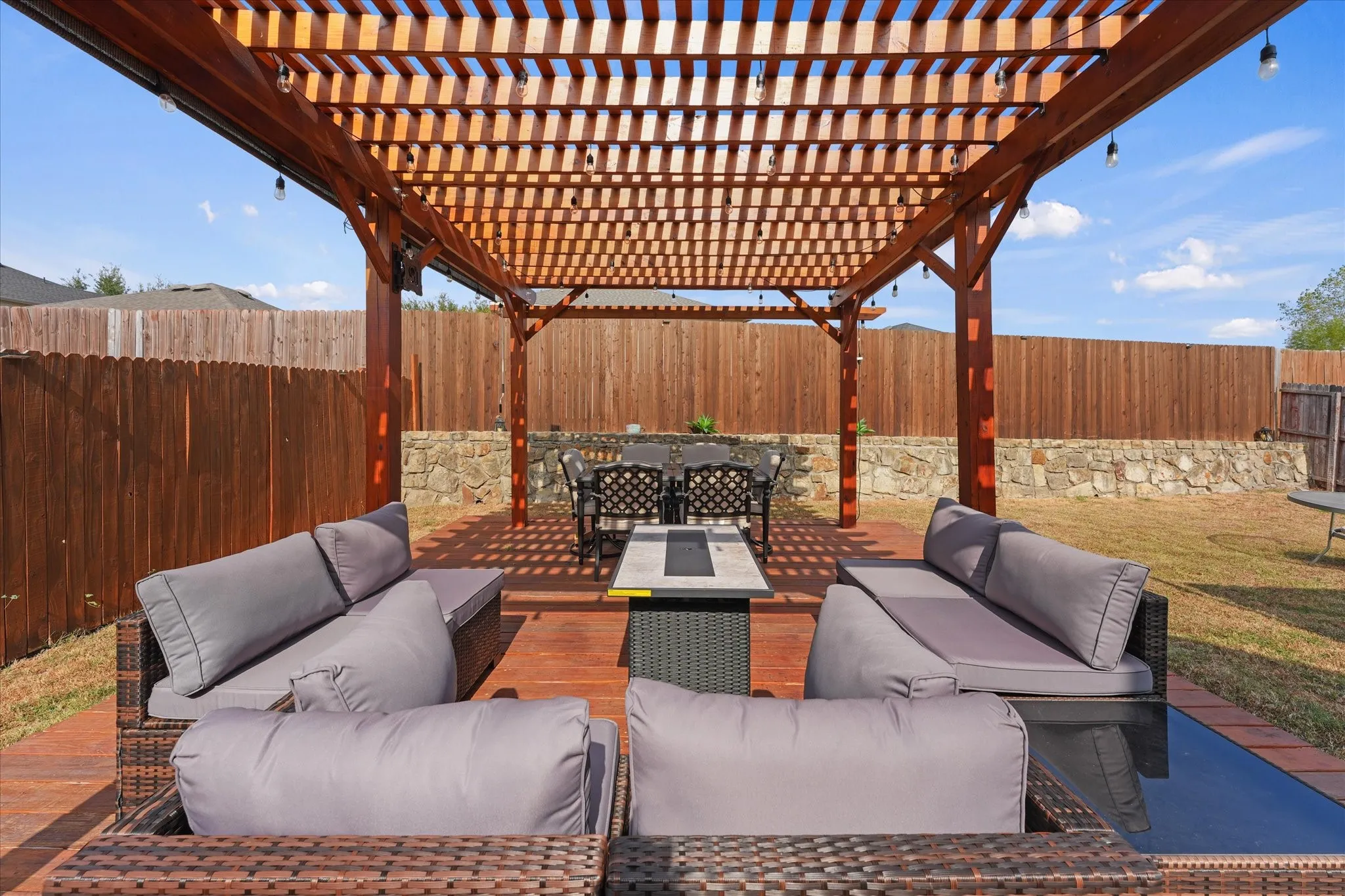 Outdoor living area featuring a wooden pergola, wood-finish deck, and stone retaining wall
