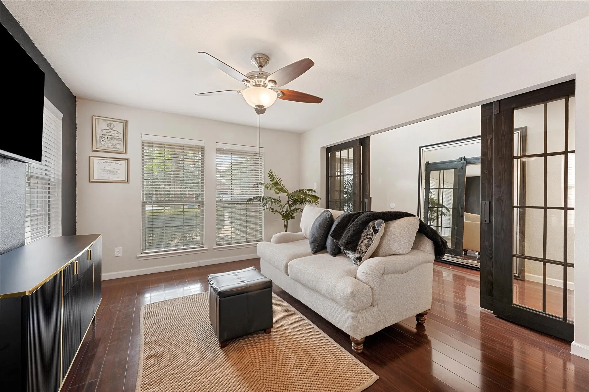 Wood-finish flooring throughout, ceiling fan with integrated lighting, and two windows with blinds