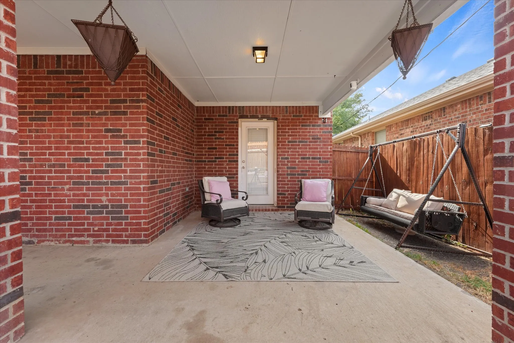 Covered concrete patio featuring brick exterior walls and a privacy fence