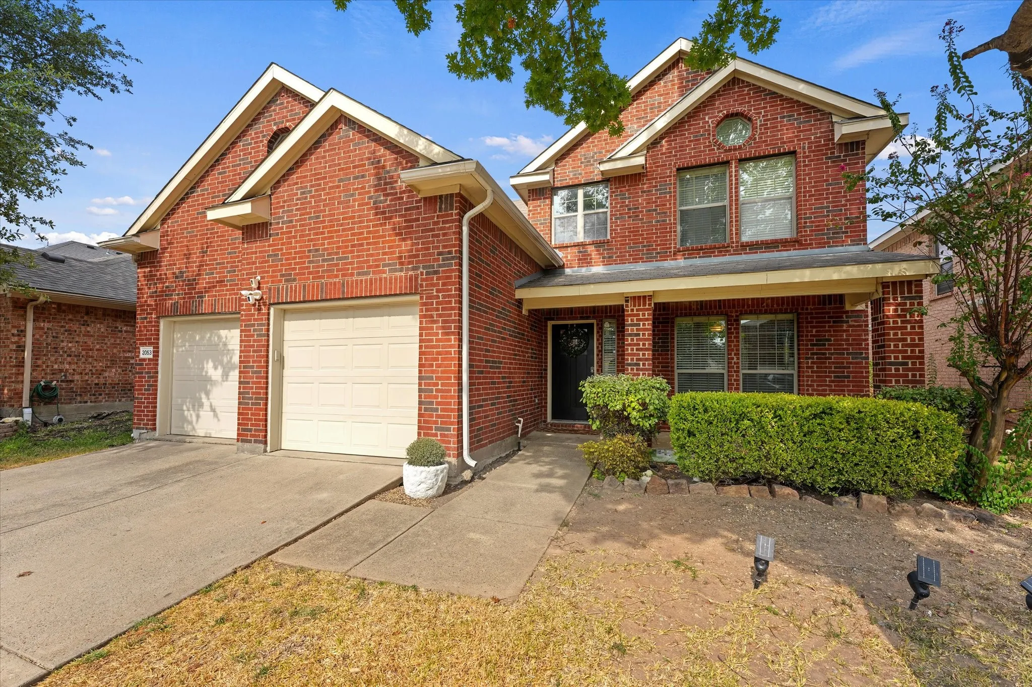 Brick exterior with a covered porch, two-car garage, and established front landscaping