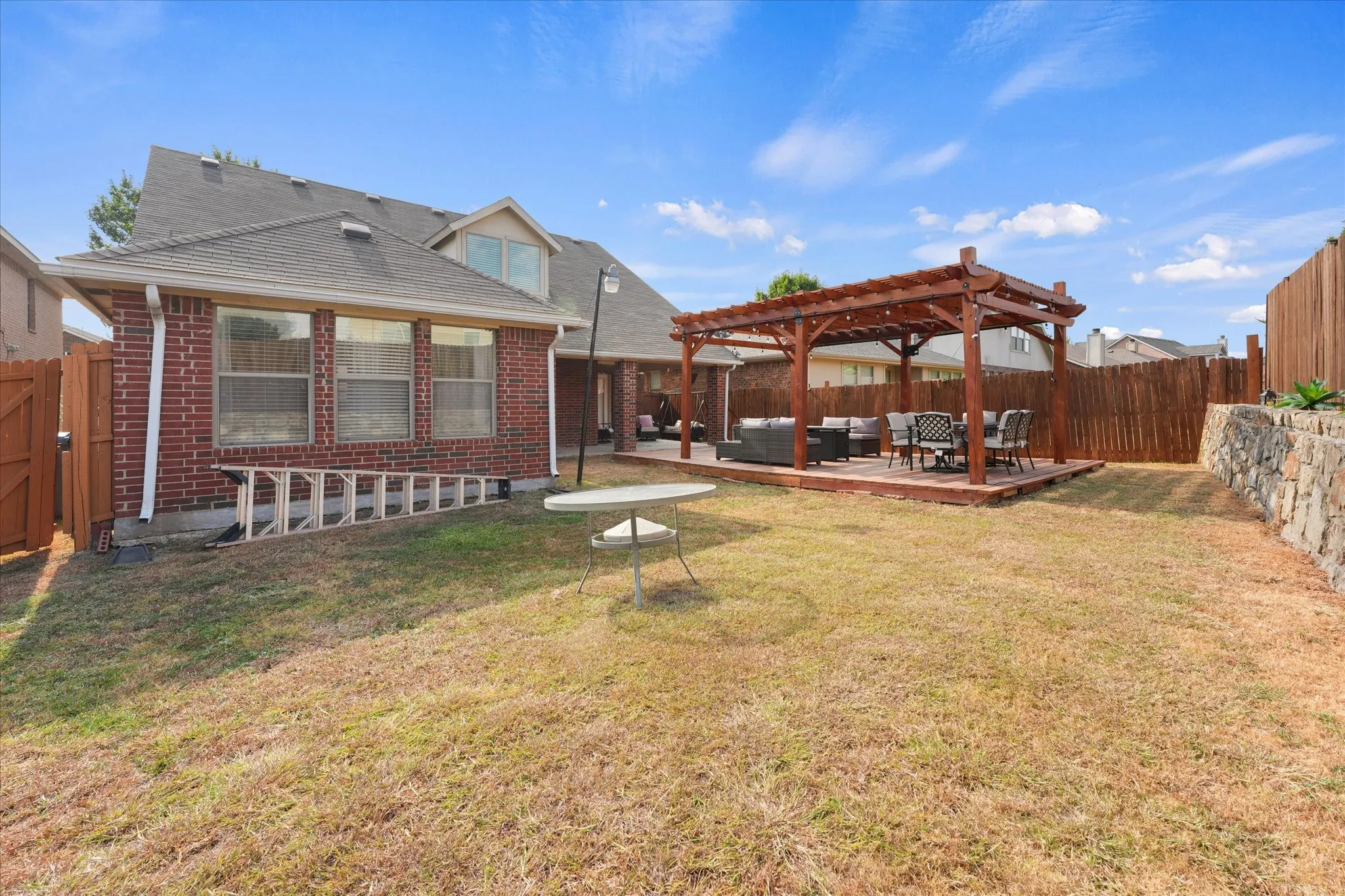 Expansive backyard featuring a wood pergola on a raised deck, a stone retaining wall, and a full privacy fence