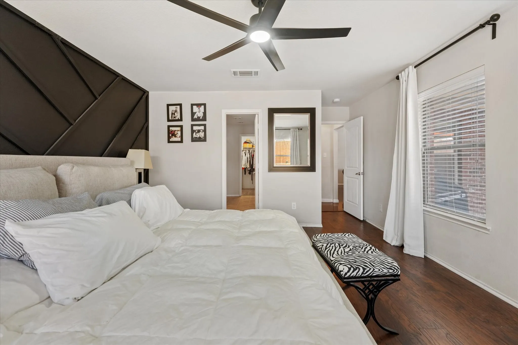 Angled geometric accent wall, wood-finish flooring, ceiling fan with integrated lighting, white window blinds, and white interior doors