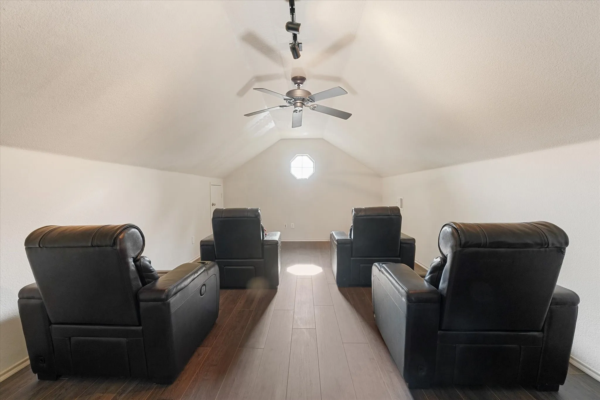 Vaulted ceiling with a ceiling fan, track lighting, wood-finish flooring, and an octagonal window