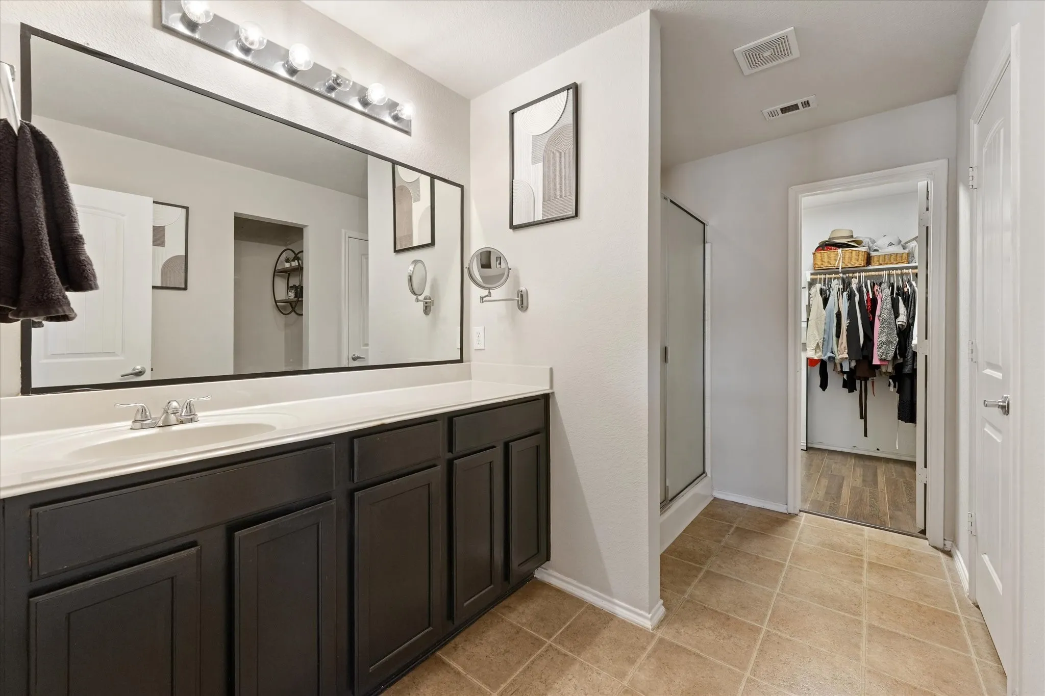 Double vanity with expansive mirror, neutral-toned cabinetry, and tiled flooring