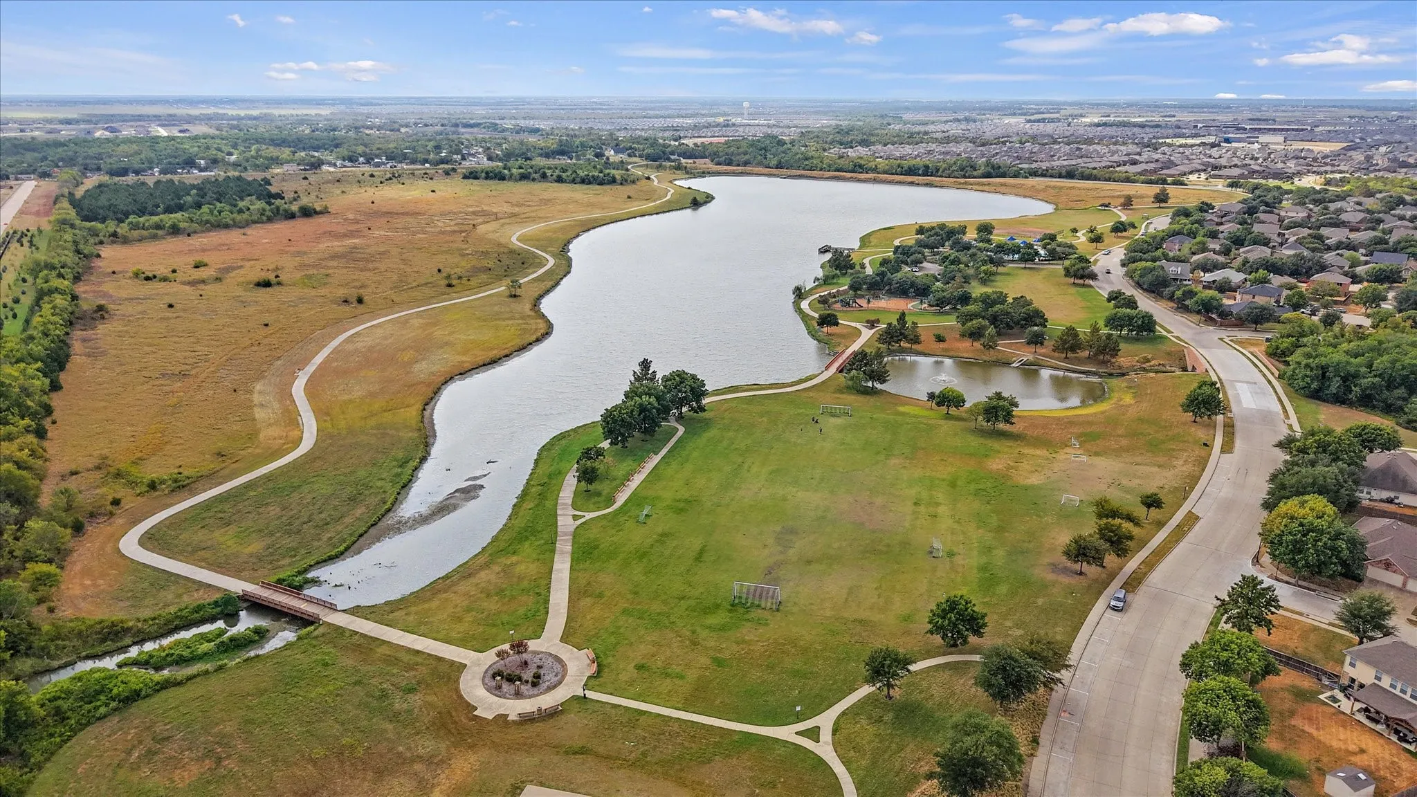 Expansive lake frontage with a pedestrian bridge, walking paths, and surrounding green spaces